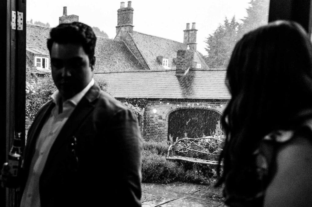 A detailed black and white image capturing a candid moment between a bride and groom at a wedding venue, with historic buildings and a garden in the background.