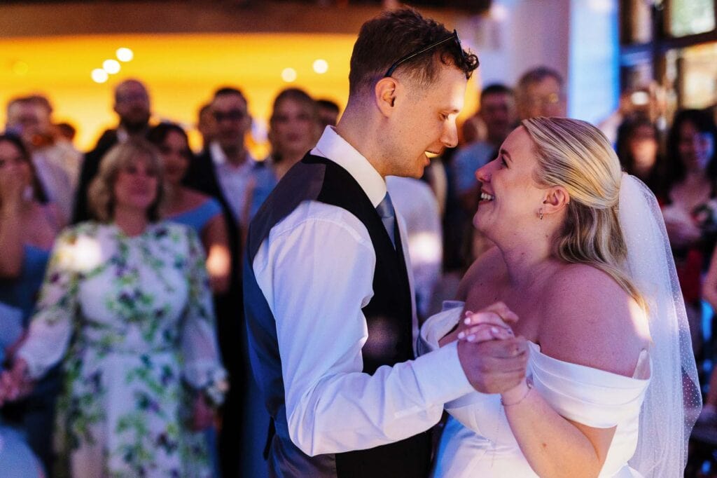 Romantic wedding dance featuring a newlywed couple with guests in the background, capturing a joyful moment at BGS Weddings in the UK.