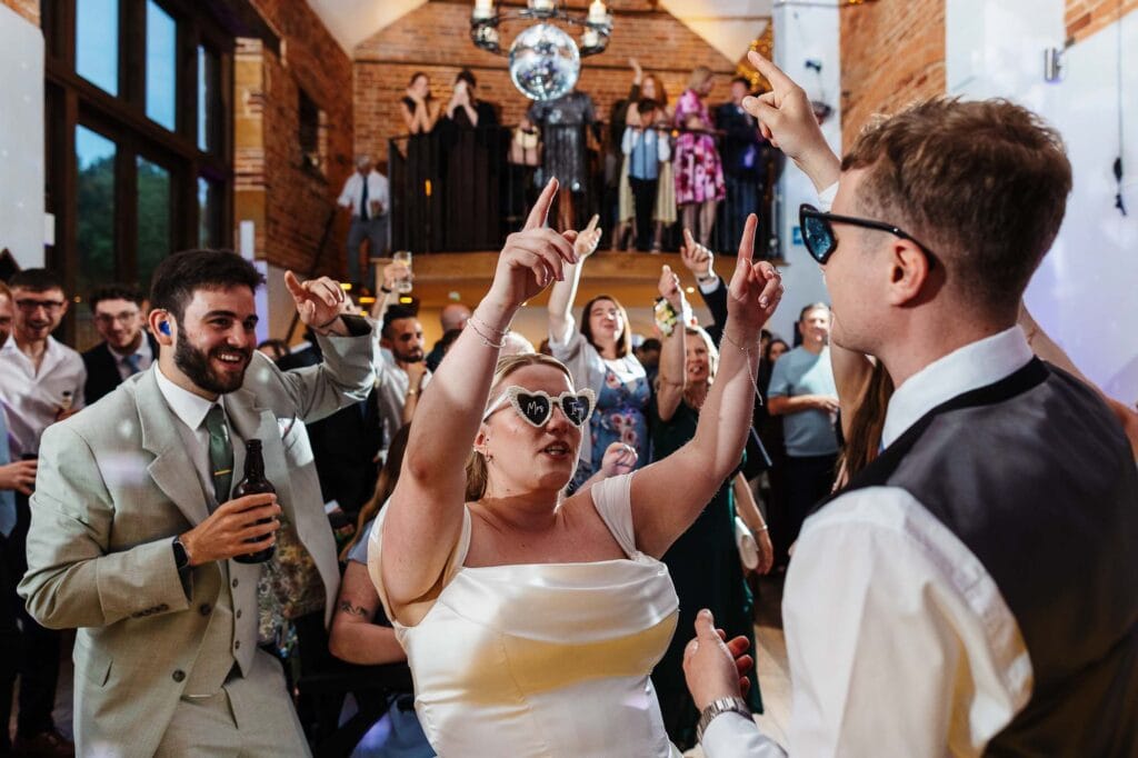 Celebrating a wedding reception with guests dancing and enjoying the party in a stylish venue with exposed brick walls and a disco ball.