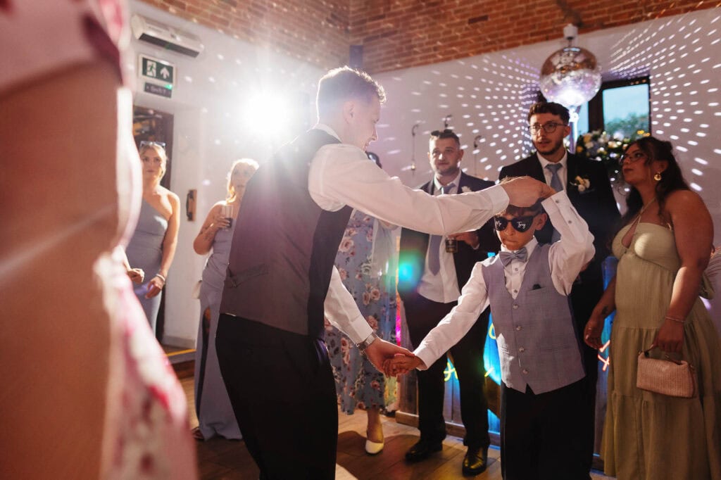 Joyful wedding reception with children dancing and adults celebrating in a stylish venue with vibrant lighting and elegant decor.