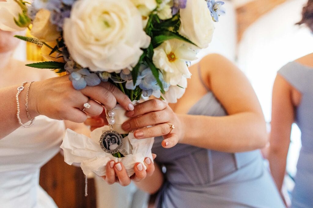 Close-up of a bride holding a bouquet of white roses and blue flowers during a wedding ceremony, with bridesmaids in the background, capturing a special moment.
