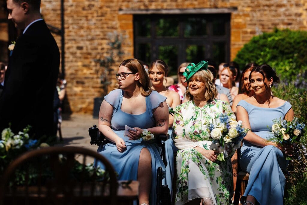 Elegant wedding ceremony with guests in blue dresses and floral arrangements outdoors at BGS Weddings, showcasing a joyful celebration.
