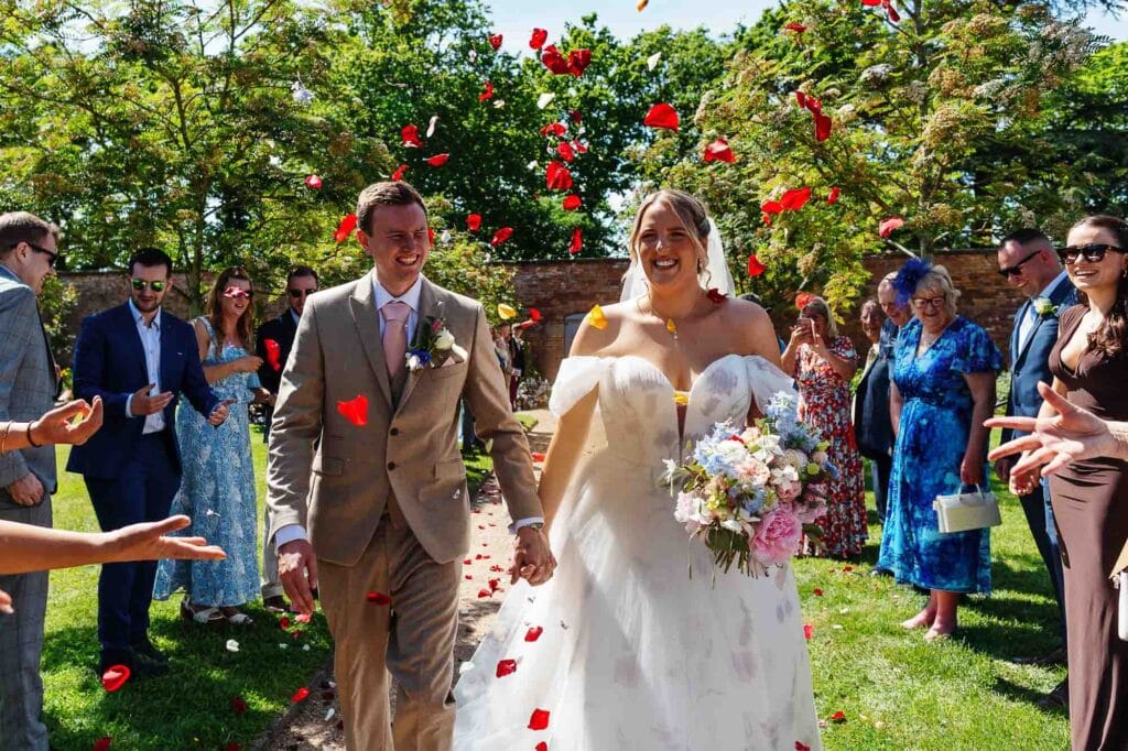 Bride and groom celebrating their wedding outdoors with friends and family, surrounded by lush greenery and vibrant flowers.