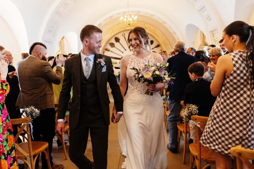 Wedding couple holding hands, smiling, and celebrating their special day in a beautifully decorated venue.