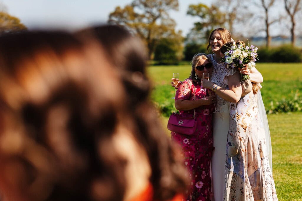 Bride holding a bouquet and smiling with guests, enjoying a joyful moment at a wedding.