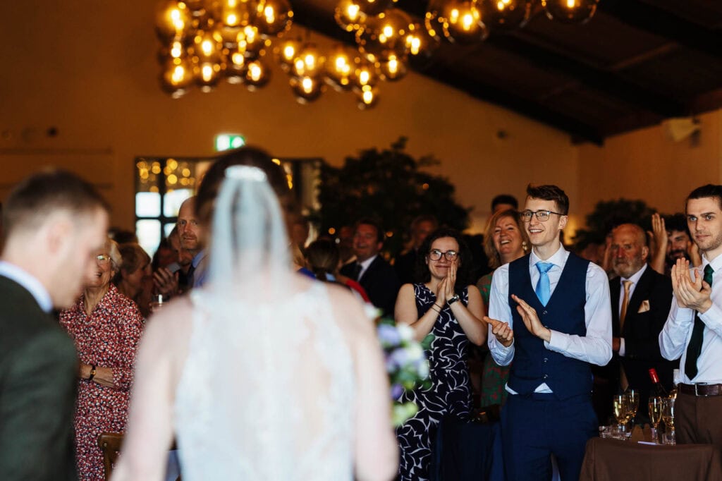Elegant wedding reception with guests clapping and celebrating the newlyweds in a beautifully decorated venue.