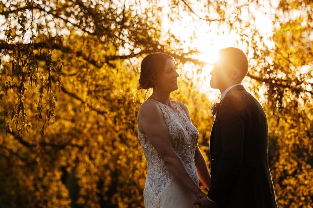 Bride and groom sharing a romantic moment outdoors during sunset, surrounded by autumn foliage, capturing love and happiness on their special day.