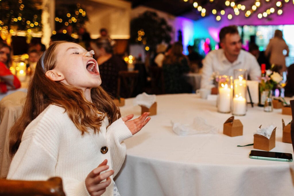 An excited young girl enjoying a joyful moment at a wedding reception, surrounded by warm candlelight and festive decorations, capturing the happiness of special celebrations.