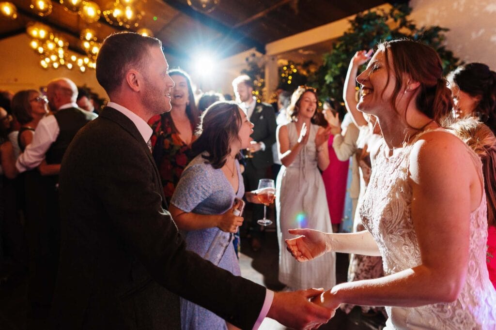 Joyful bride and groom dancing at their wedding reception with guests celebrating in a beautifully decorated venue.