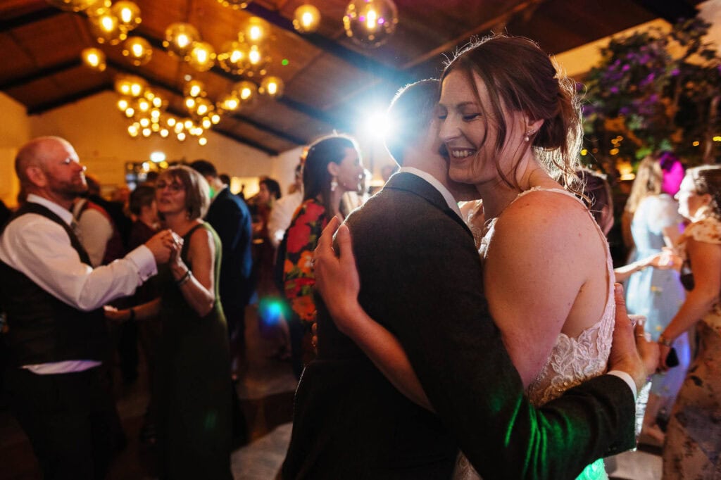 Happy bride and groom sharing a romantic dance at their wedding reception, surrounded by joyful guests and warm lighting, capturing a special moment of celebration.