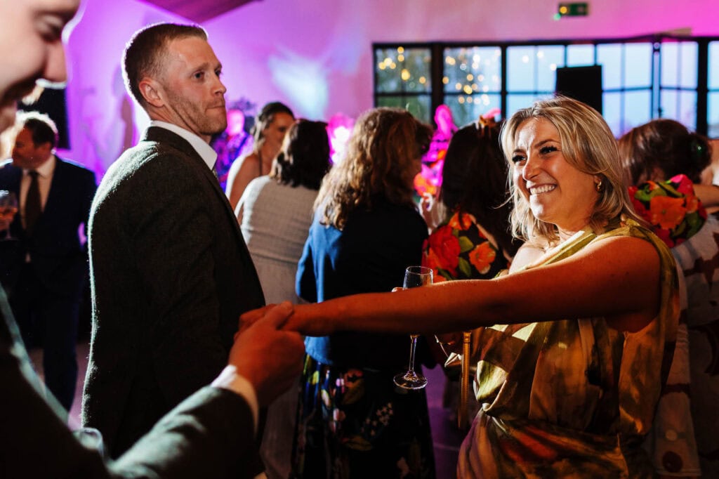 Happy couple dancing and celebrating at a wedding reception with guests, colourful lighting, and joyful atmosphere.