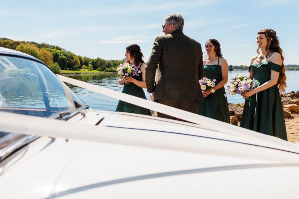 Beautiful outdoor wedding scene featuring bridesmaids holding bouquets, officiant, and scenic river backdrop.