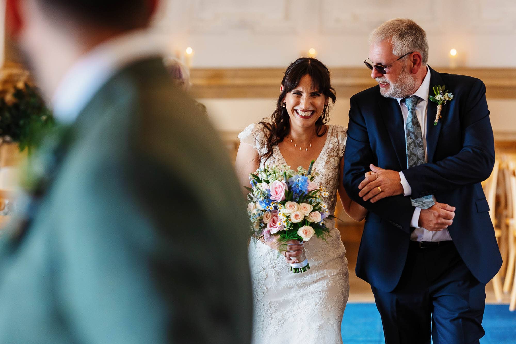 Wedding ceremony at BGS Weddings, happy bride holding a bouquet, walking down the aisle with her father in a beautiful indoor setting.