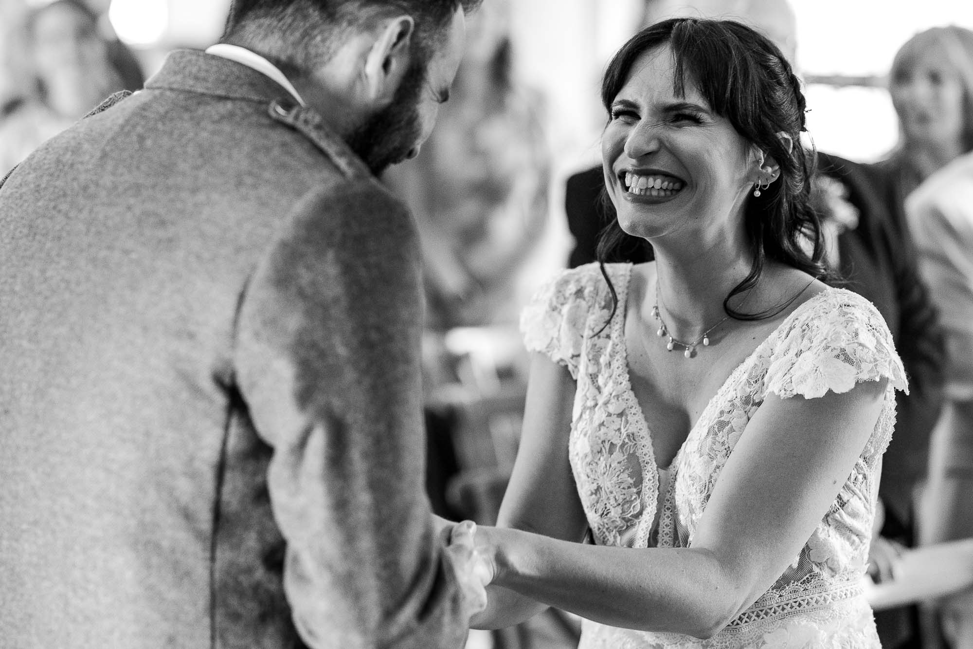 Bride smiling happily while holding groom's hands during wedding vows.