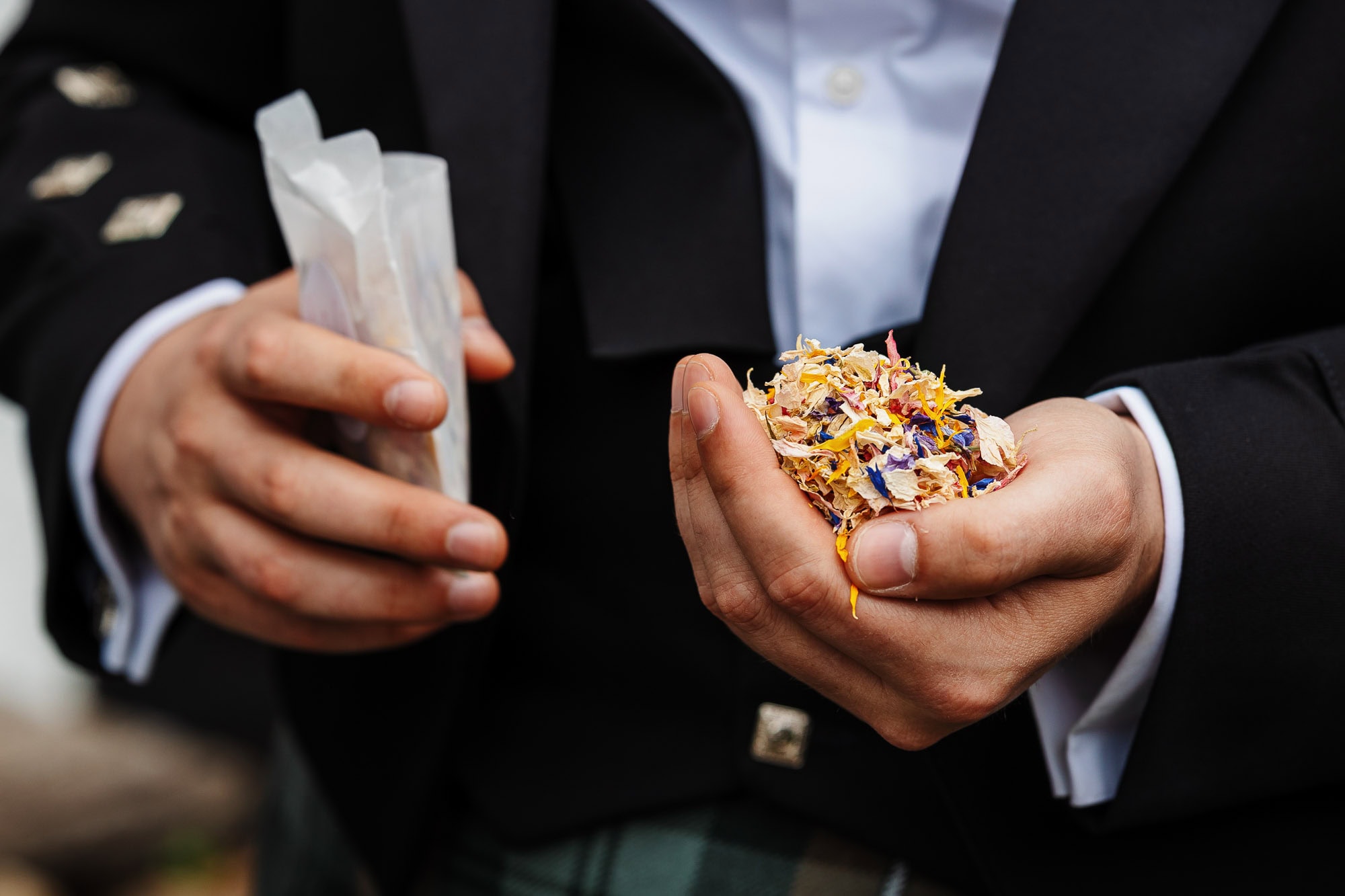 Close-up of groom holding colorful flower petals and confetti at a wedding, ready for celebration.