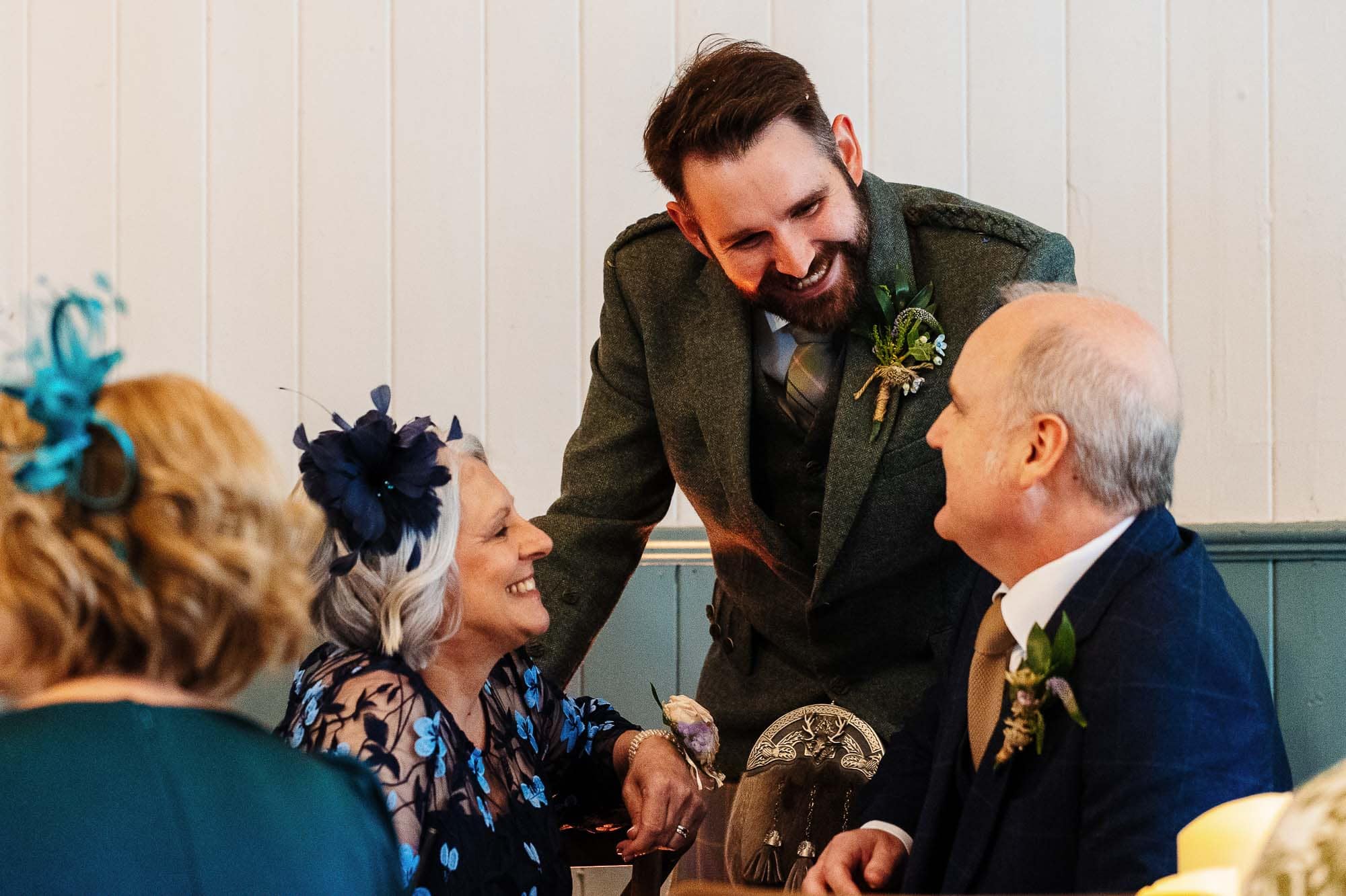 A candid moment at a wedding reception showing guests sharing a joyful conversation, with a focus on a smiling woman and an elderly man, capturing the warmth and happiness of the special day.